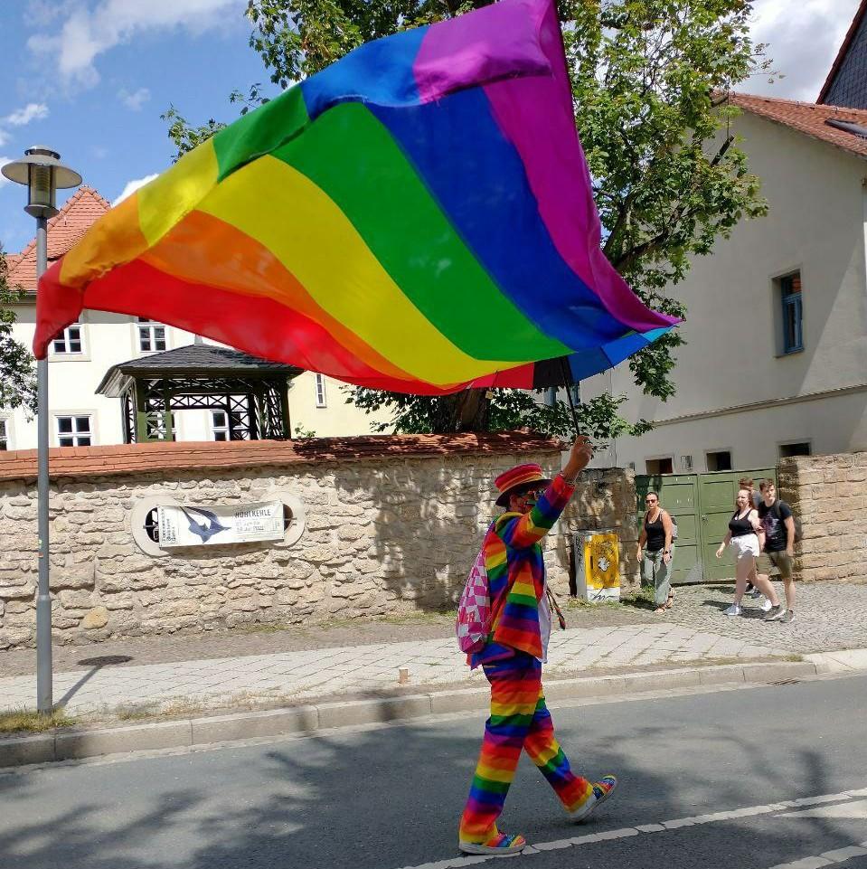 Symbolbild: Juni ist Pride Month (Person in Regenbogen-Kleidung schwenkt große Regenbogenfahne)